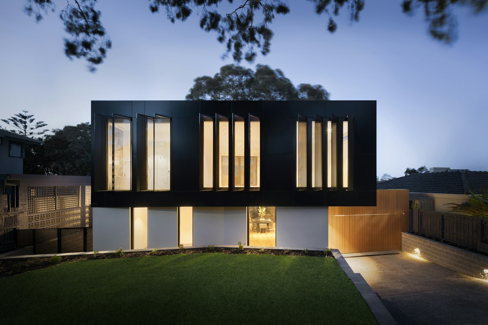 Two-story house at blue hour with warm window light and the building form readable against the evening sky
